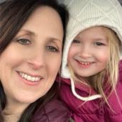 Woman with a winter coat is taking a selfie with a young child wearing a winter coat and hat.