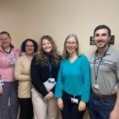 A group of five people stand side-by-side in the hallway of a clinic and are smiling at the camera.