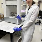 Woman in a white lab coat in a research lab holding a syringe and about to place a sample in a collection tray.