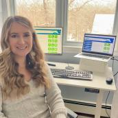 Woman with long, blonde, wavy hair smiles at the camera, home office in the background.