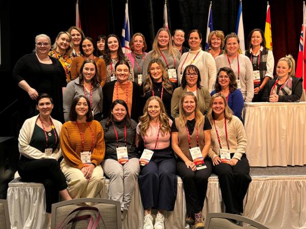 Group of 25 nurses smiling on a stage.