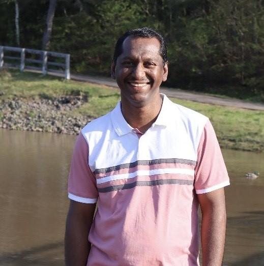 Headshot of Philip Chandy, smiling, outdoor in front of a pond