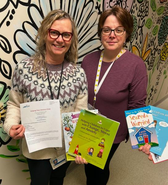 Two adult females standing facing camera holding educational literature.