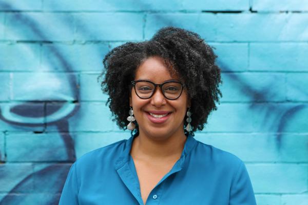 o	Photo of smiling woman (Stephanie Bizzeth) wearing glasses in a blue shirt in front of a blue background.