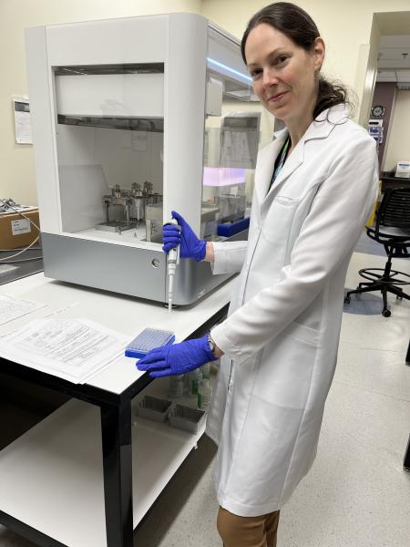 Woman in a white lab coat in a research lab holding a syringe and about to place a sample in a collection tray.