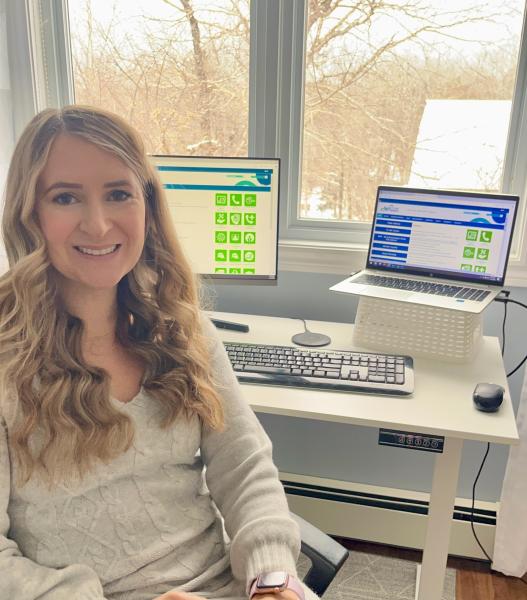 Woman with long, blonde, wavy hair smiles at the camera, home office in the background.