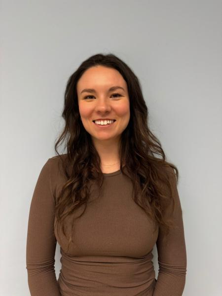 Woman with long brown hair wears a brown long-sleeve shirt and is smiling at the camera.